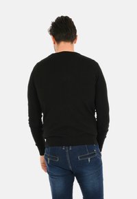 Maglione nero a maglia con scollo tondo, polsini e orlo a coste, abbinato a jeans in denim blu con tasche posteriori e dettagli di cucitura.