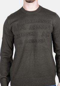 Felpa verde oliva con collo a giro e maniche lunghe. Presenta un testo del marchio in rilievo sulla parte anteriore. Tessuto morbido, design aderente.