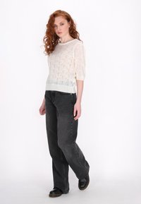 Maglione bianco semitrasparente lavorato a maglia con maniche corte, abbinato a jeans neri a vita alta e larghi e scarpe nere.
