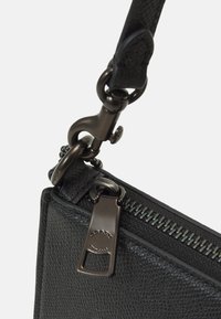 Nærbillede af hjørnet af en sort struktureret lædertaske med metallynlås og lås på en aftagelig rem.