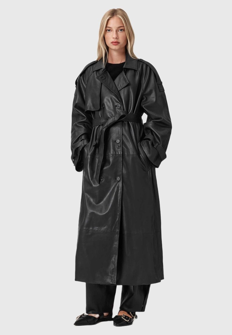 Cappotto trench in pelle nera con vestibilità oversize, davanti doppiopetto, ampi revers e cintura. Presenta tasche laterali e una texture liscia.