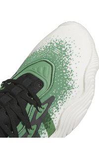 Chaussure de sport blanche et verte avec des lacets noirs, une semelle texturée et un motif vert pixellisé près de la zone des orteils.
