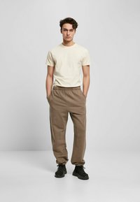 Kremfarget t-skjorte med kort erm, kombinert med løse brune joggebukser med elastisk linning og svarte snøresko.
