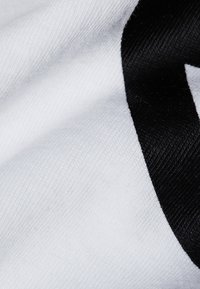 T-shirt met een witte stof met een gladde textuur en een dikke zwarte stripe erop. De stof lijkt kreukvrij en lichtgewicht te zijn.