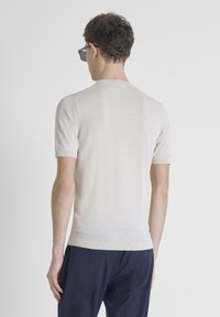 Maglione a maniche corte beige in maglia con scollo rotondo, orlo a costine e texture liscia. Design minimalista, abbinato a pantaloni navy scuri.