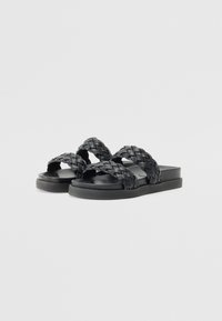 Sorte svarte sandaler med tverrvevde stropper laget av syntetisk materiale, flat såle og minimalistisk design uten ekstra dekorasjoner.