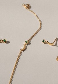 Goldfarbener Schmuckset, bestehend aus einem Kettenarmband mit einem Halbmondakzent und passenden Ohrringen, die mit grünen Edelsteindetails versehen sind.