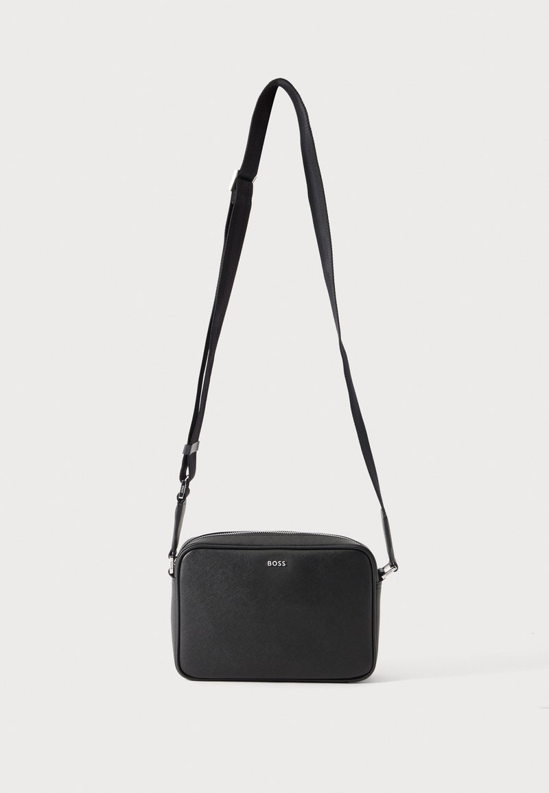 Sac bandoulière rectangulaire noir avec sangle réglable et logo BOSS sur le devant, sur un fond clair uni.