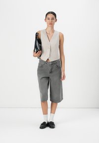 Gilet a coste beige con bottoni, pantaloni corti in denim grigio, calzini bianchi, mocassini neri e borsa nera in mano. Design semplice e moderno.