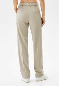 Lichtbeige, op maat gemaakte broeken met een rechte pijp, riemlussen, achterzak en een gladde stofstructuur, gecombineerd met witte sneakers.