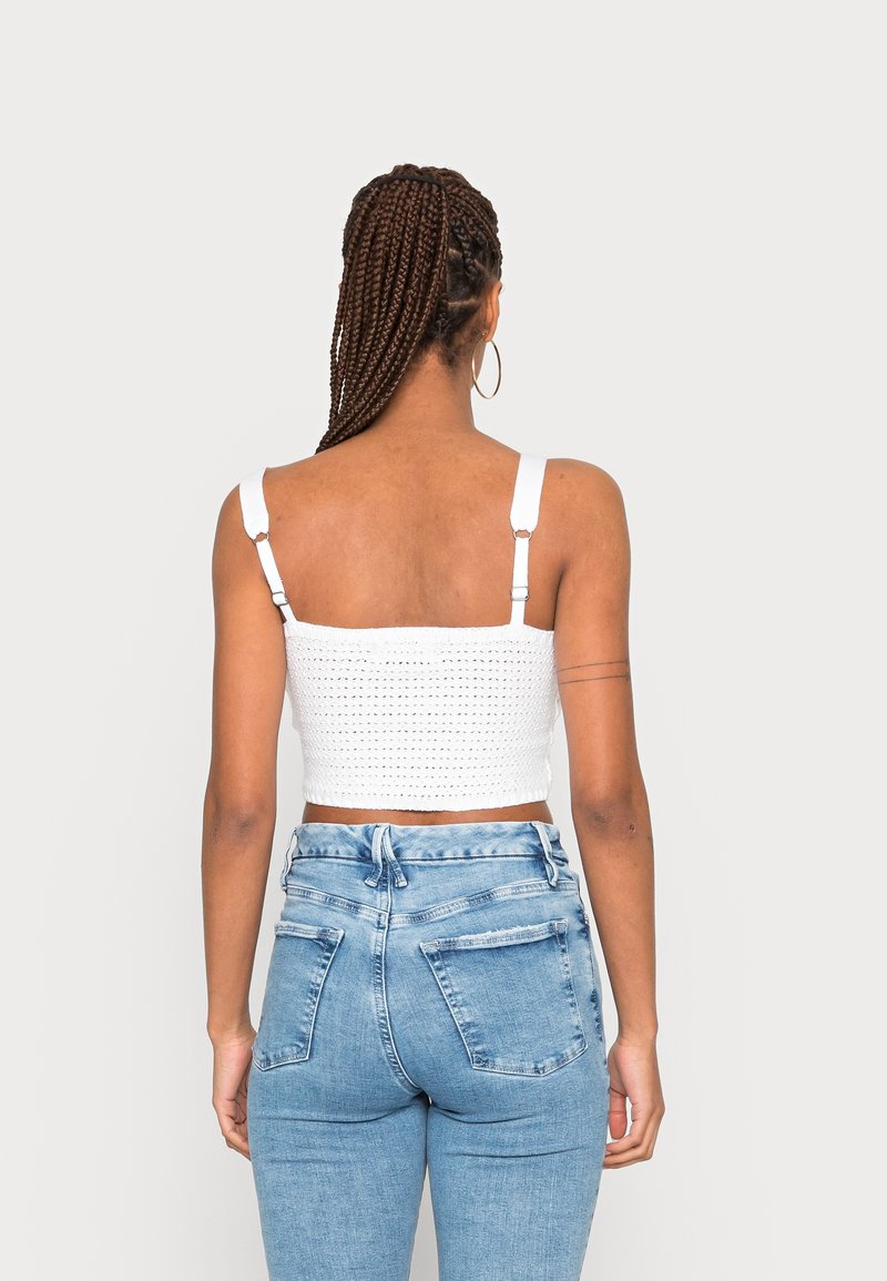 Top corto de ganchillo blanco con tirantes ajustables, combinado con jeans de mezclilla azul de cintura alta, que cuentan con bolsillos delanteros y traseros.