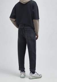 Jeans de mezclilla negros con un corte relajado y dobladillo deshilachado, combinados con una sudadera oscura. Zapatillas gris y azul completan el conjunto, mostrando un estilo casual.