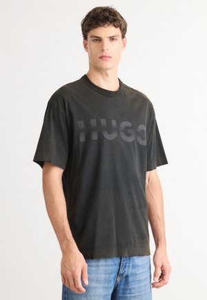 Black cotton t-shirt with a crew neck, featuring a large, tonal "HUGO" logo. Loose fit with short sleeves and a soft texture.