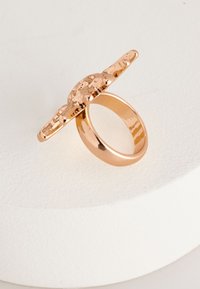 A rose gold ring with a textured, wide top and smooth band, featuring a decorative, raised pattern on the surface.