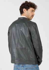 Grijs leren jack met een eenvoudig ontwerp, voorzien van een staande kraag, gestikte details en een zachte textuur, gedragen over blauwe jeans.