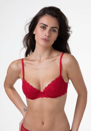Reggiseno in pizzo rosso con sottili spalline, caratterizzato da motivi floreali e un bordo ondulato lungo le coppe. Il tessuto ha una consistenza morbida.