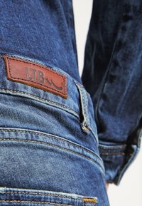 Denimjeans med en mörkblå tvätt, med en brun läderlapp märkt "LTB" och subtila sömnadsdetaljer. Standard passform.