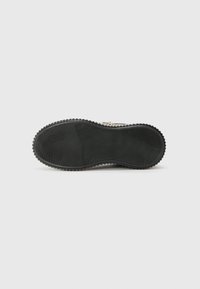 Svart såle med dype spor og en teksturert overflate. Runde kanter og lett hevede rygger gir trekk og grep.
