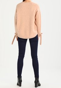 Ljusrosa oversized tröja med texturerat tyg, rund halsringning och knytband vid ärmarna, tillsammans med mörkblå skinny jeans och ankelboots.