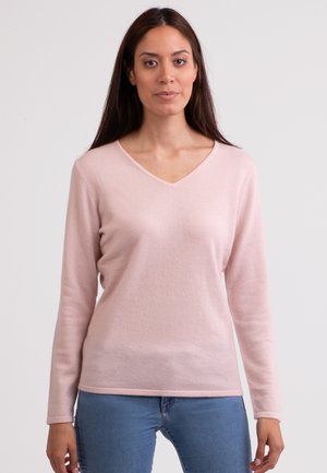 Lichtroze v-hals trui gemaakt van zachte, getextureerde stof met lange mouwen en een losse pasvorm, gecombineerd met blauwe denim jeans.