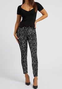 Top negro de manga corta con escote en forma de ronda, combinado con jeans ajustados negros que presentan un patrón de rayas onduladas plateadas. Zapatos de tacón alto.