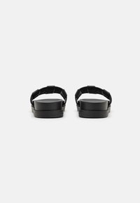 Black sandals with a flat sole, featuring a wide strap design. The material appears smooth with a matte finish. No visible patterns or accents.