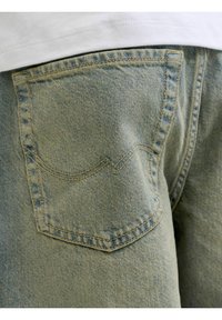Světle modré džíny z denimu s zadní kapsou a zakřiveným steh. Materiál má texturovaný povrch a vybledlé oblasti.