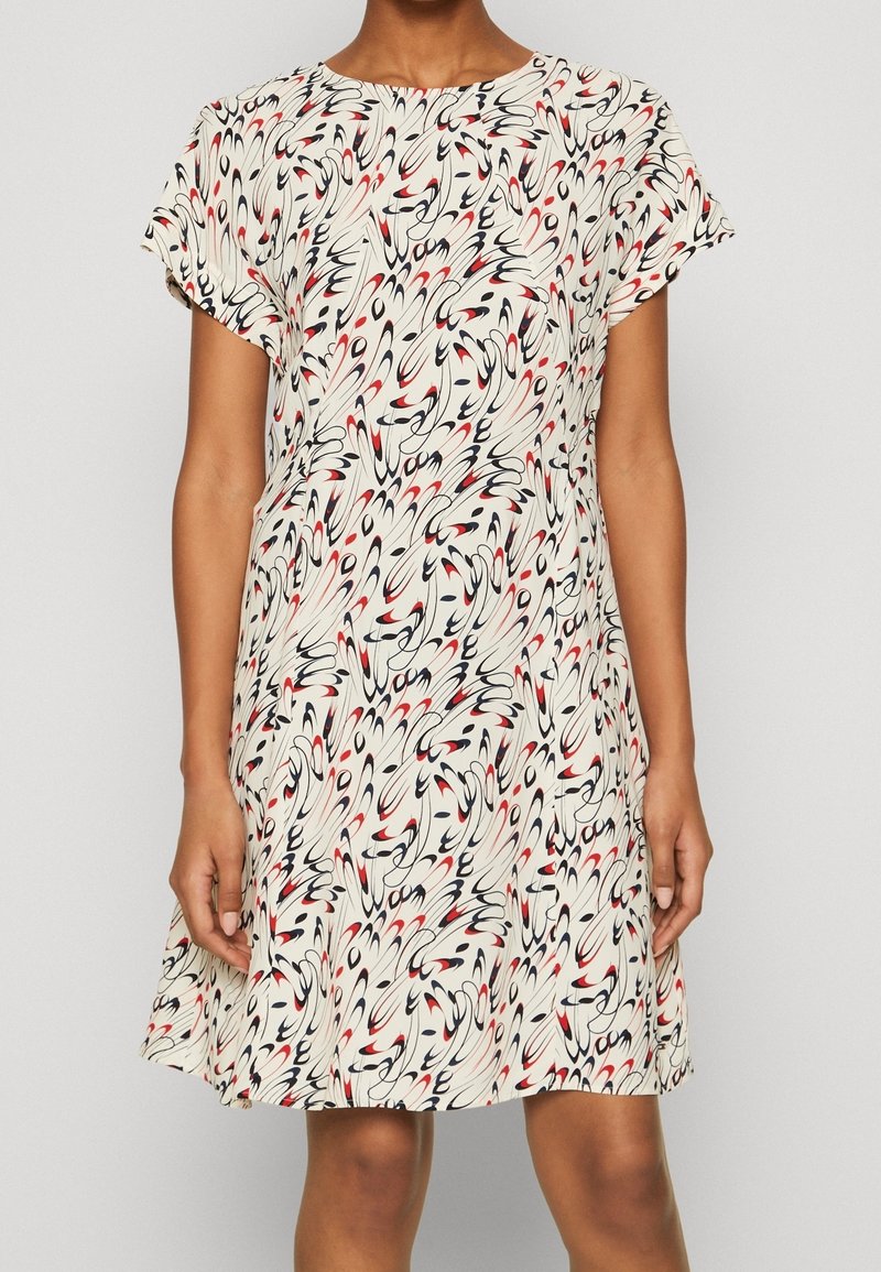 Femme portant une robe à manches courtes, longueur genou, base crème avec un motif abstrait en spirales noires et rouges.