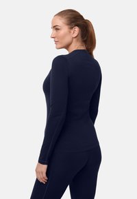 Marineblaues Langarmshirt mit tailliertem Schnitt, glatter Textur und rundem Ausschnitt. Akzente setzen dezente Nähte entlang der Nähte.