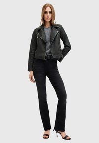 Giacca da biker in pelle nera con spalle trapuntate, maglione grigio e jeans neri a zampa d'elefante, completato con sandali neri con tacco.