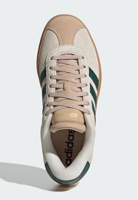 Sneakers Adidas con una toma in suede beige, strisce in pelle verde, linguetta in rete color crema e dettaglio del logo dorato sul tallone.