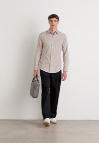 Lys beige skjorte med knapper, sorte bukser og hvite sneakers. Holder en grå veske med håndtak. Minimalistisk design. Glatte teksturer.