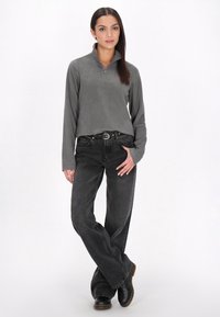 Grijze fleece pullover met een halve rits kraag, gecombineerd met zwarte wijde jeans en zwarte laarzen, wat een casual outfit laat zien.