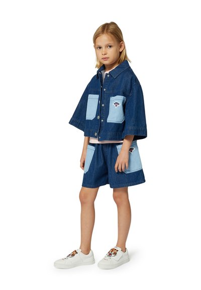 Denim jack met korte mouwen en lichtblauwe zakken, gecombineerd met bijpassende shorts. Witte sneakers hebben een tijgerontwerp.