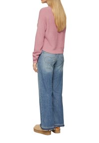 Roze gebreide trui met een ontspannen pasvorm, gecombineerd met lichtblauwe broek met wijde benen en rafelige zomen, en beige platformschoenen.