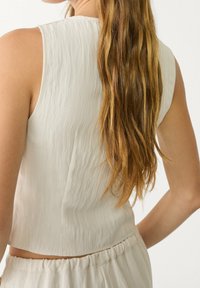 Light beige sleeveless top with a textured fabric, cropped design, and a round neckline, paired with matching elastic waistband bottoms.