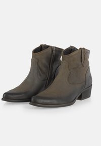 Botas de cuero marrón hasta el tobillo con una textura suave, punteras puntiagudas, costuras decorativas y cremalleras laterales. Los tacones apilados mejoran la estabilidad.