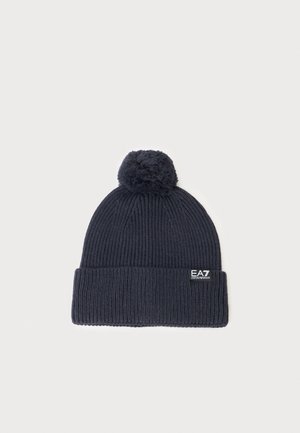 Bonnet en maille côtelée bleu marine foncé avec un revers plié, surmonté d'un pompon, et un petit patch logo EA7 Emporio Armani sur le revers.