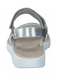 Sandalias con tiras metálicas plateadas que cuentan con una plantilla acolchada de color beige y una suela blanca ligera con textura. Diseño de talón abierto con tira ajustable.