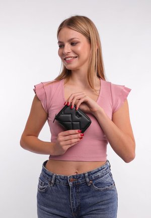 Black textured wallet with a diamond pattern and zip closure, held in hand against a light background, paired with a pink top and denim jeans.