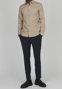 Beige skjorta med lång ärm och knäppning, ihop med mörk marinblå slim-fit byxor och svarta slip-on skor.