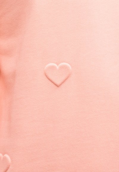 Μαλακό ροζ ύφασμα με ανάγλυφα σημάδια καρδιών στο υλικό, δημιουργώντας ένα διακριτικό υφασμένο μοτίβο.