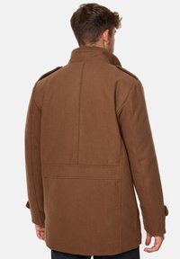 Abrigo de mezcla de lana marrón con cuello alto, hombros estructurados y bolsillos traseros. Presenta una textura suave y un ajuste entallado.