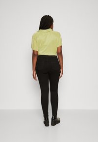 Žalia raištinė trumpa rankovė marškinė, derinama su juodomis aukštomis džinsinėmis kelnėmis. Juodi platforminiai batai užbaigia aprangą.