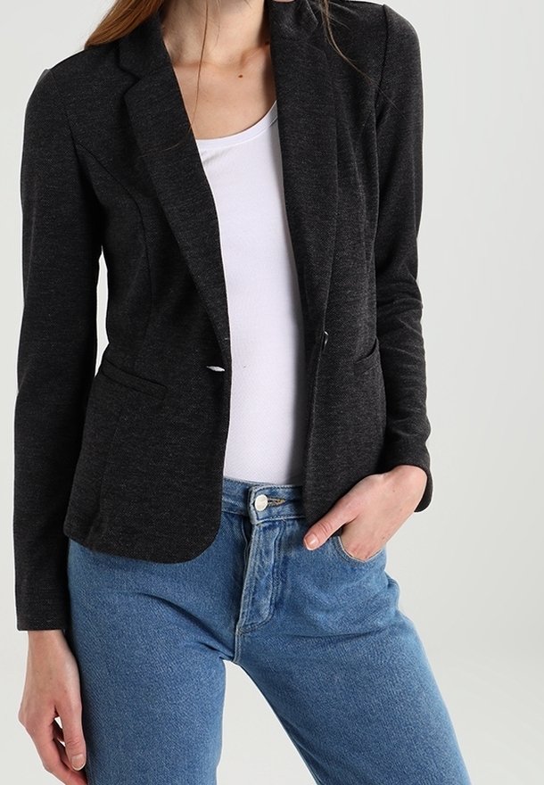 Blazer gris foncé avec des revers crantés, deux poches avant et une coupe ajustée, associé à une chemise blanche et un jean bleu clair.