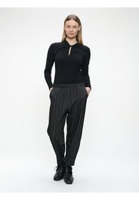 Schwarzes Langarmoberteil mit einem Schlüsselloch-Detail, kombiniert mit grauen Nadelstreifen-Hosen. Die Hosen haben einen lockeren Schnitt und Seitentaschen.