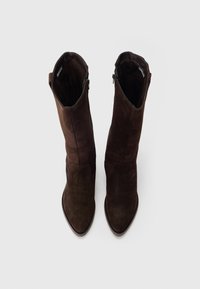 Botas de ante marrón hasta la rodilla con punta puntiaguda y detalles sutiles de costuras, con una cremallera en el lado interior para el cierre.