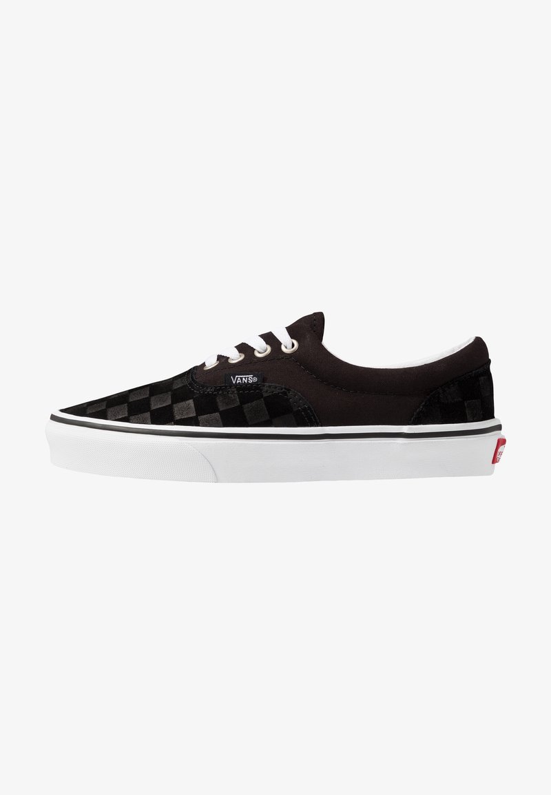 Baskets basses Vans noires avec lacets blancs, motif à damier à l'avant et à l'arrière, et semelle en caoutchouc blanche avec logo Vans rouge.