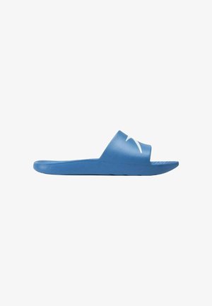 Sandalo blu slip-on con ampia fascia che presenta un logo bianco stilizzato sulla parte superiore, visto di lato su sfondo bianco.
