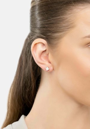 Silver stud earrings with a square, clear cubic zirconia design, showcased against a neutral background, worn on a model's ear.